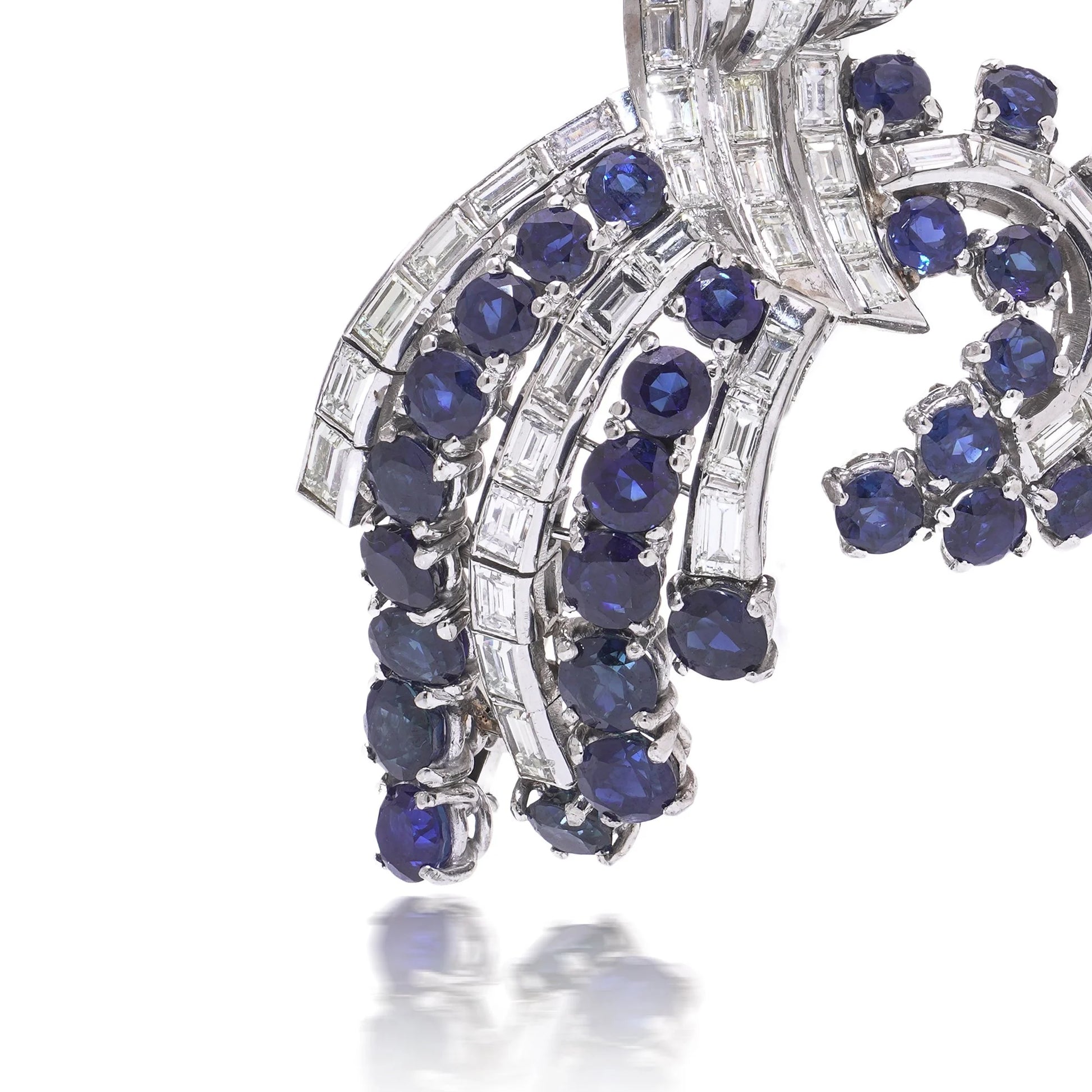 A decorative baguette cut diamond and round sapphire brooch in white metal, on a white background