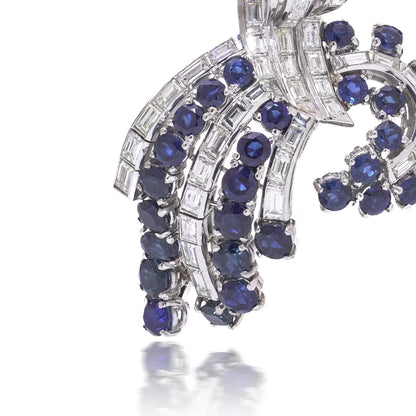 A decorative baguette cut diamond and round sapphire brooch in white metal, on a white background