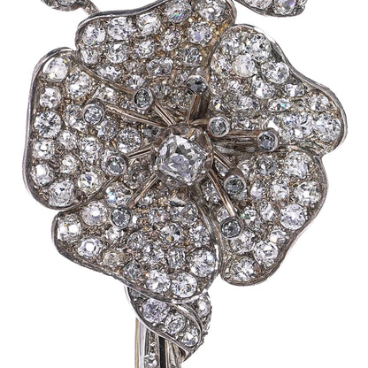 A decorative flower brooch set with diamonds, in silver and gold, on a white background