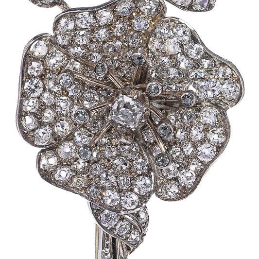 A decorative flower brooch set with diamonds, in silver and gold, on a white background
