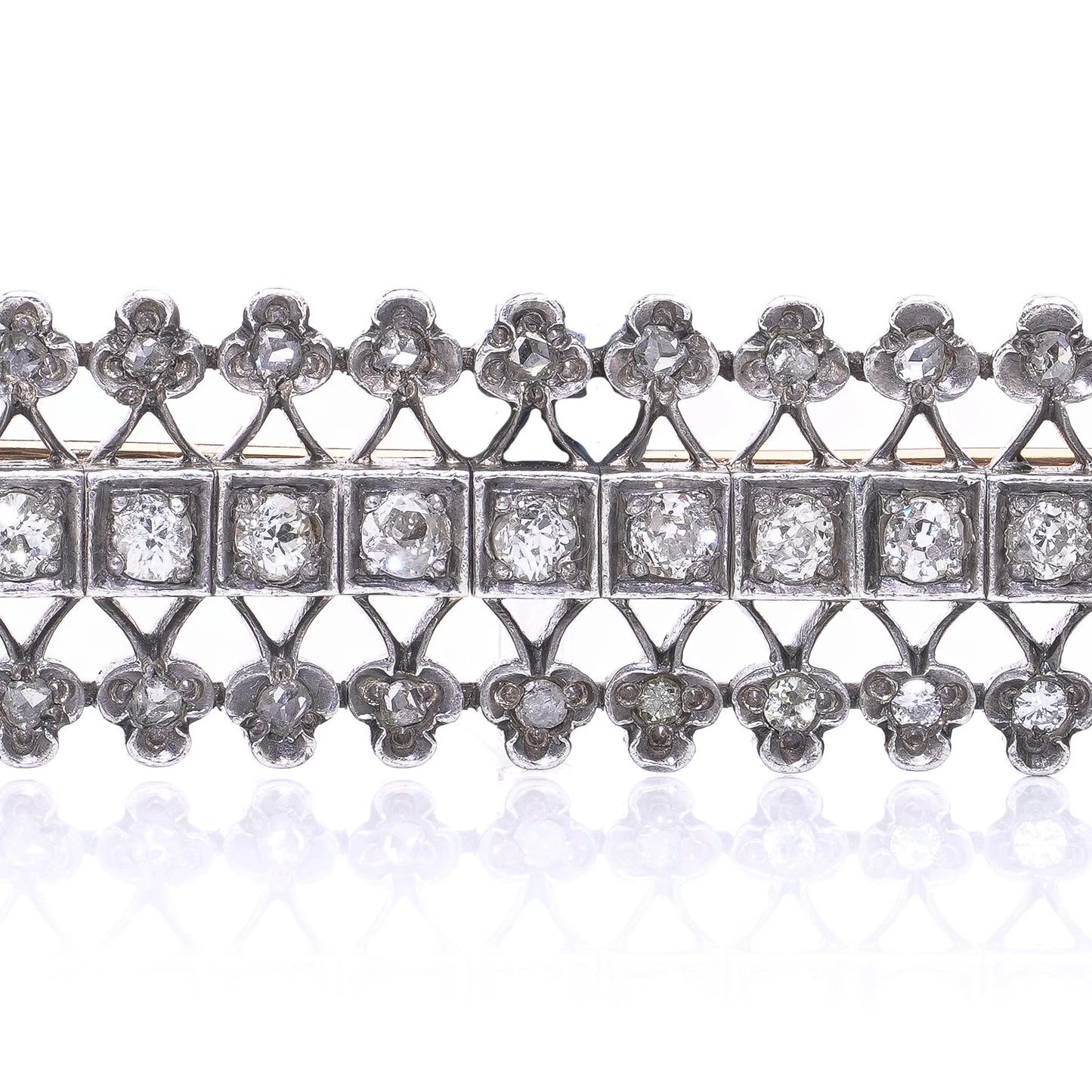 An openwork diamond set bar brooch in gold and silver, on a white background
