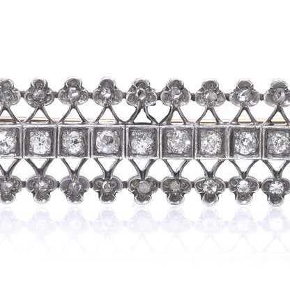 An openwork diamond set bar brooch in gold and silver, on a white background
