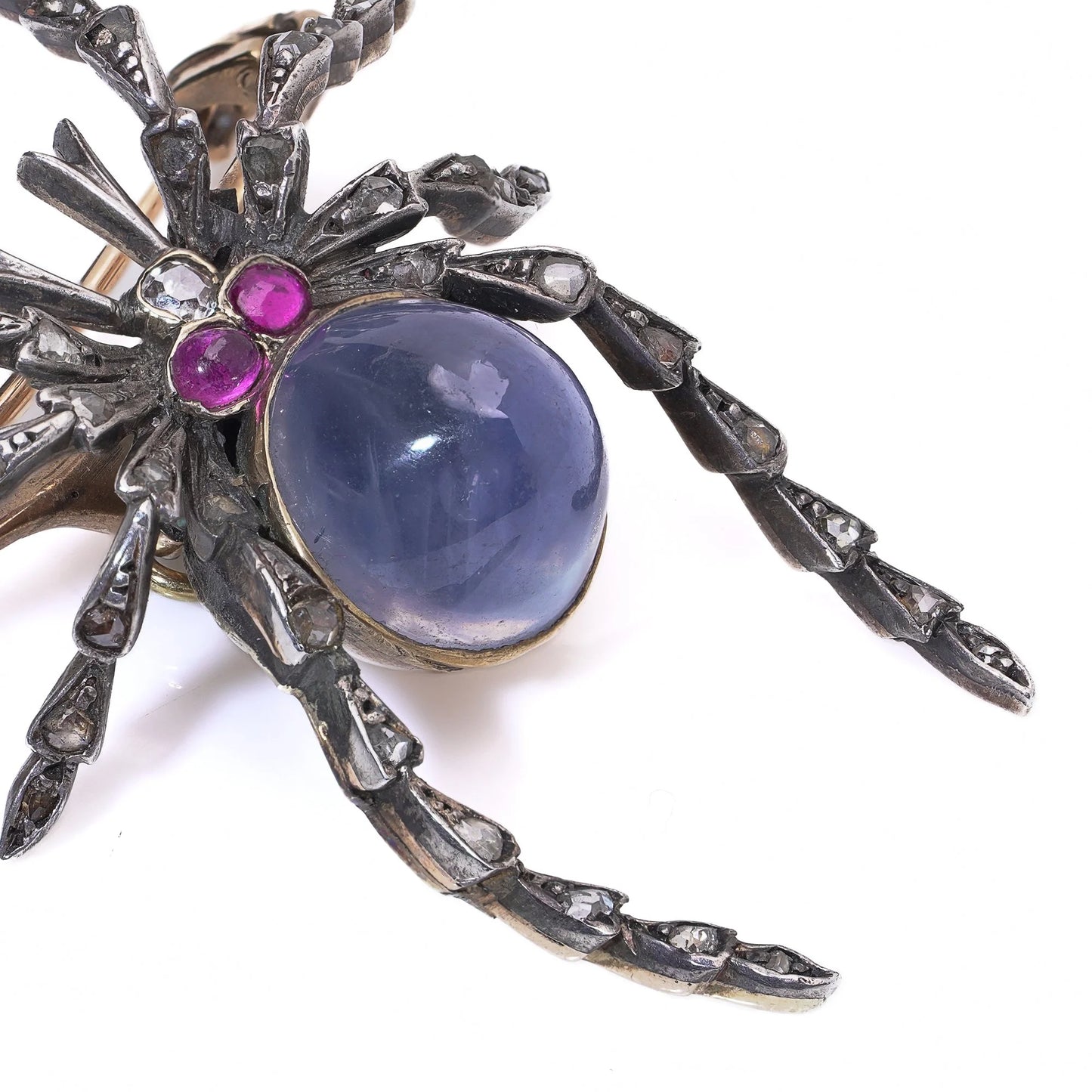 A spider brooch with a sapphire and ruby body and diamond legs, in silver and gold, on a white background