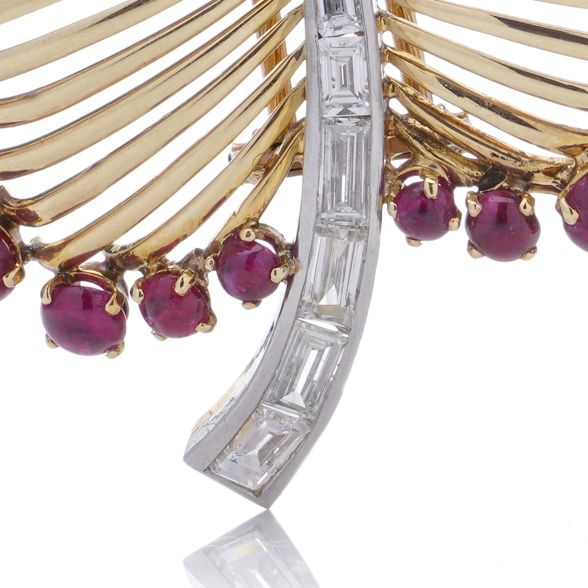 A gold and platinum leaf shaped brooch with baguette cut diamonds and cabochon cut rubies, on a white background
