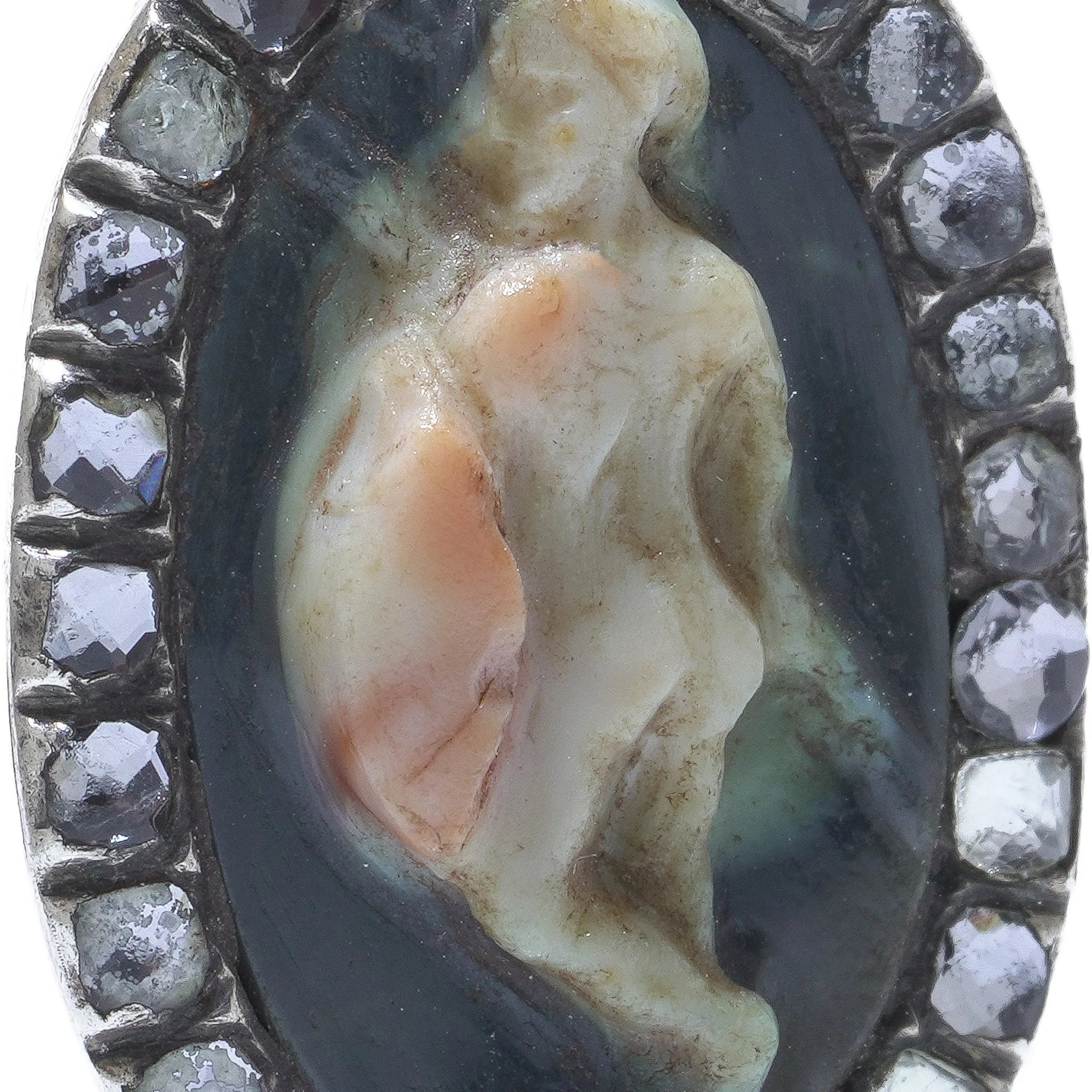 An oval cameo brooch depicting a nude figure, with diamonds around the border, on a white background