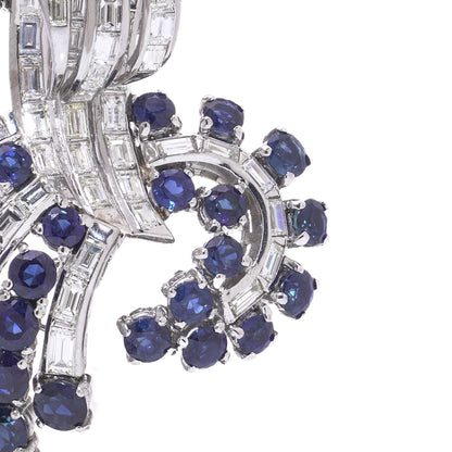 A decorative baguette cut diamond and round sapphire brooch in white metal, on a white background