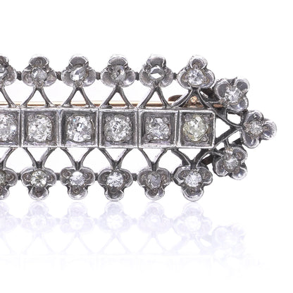 An openwork diamond set bar brooch in gold and silver, on a white background