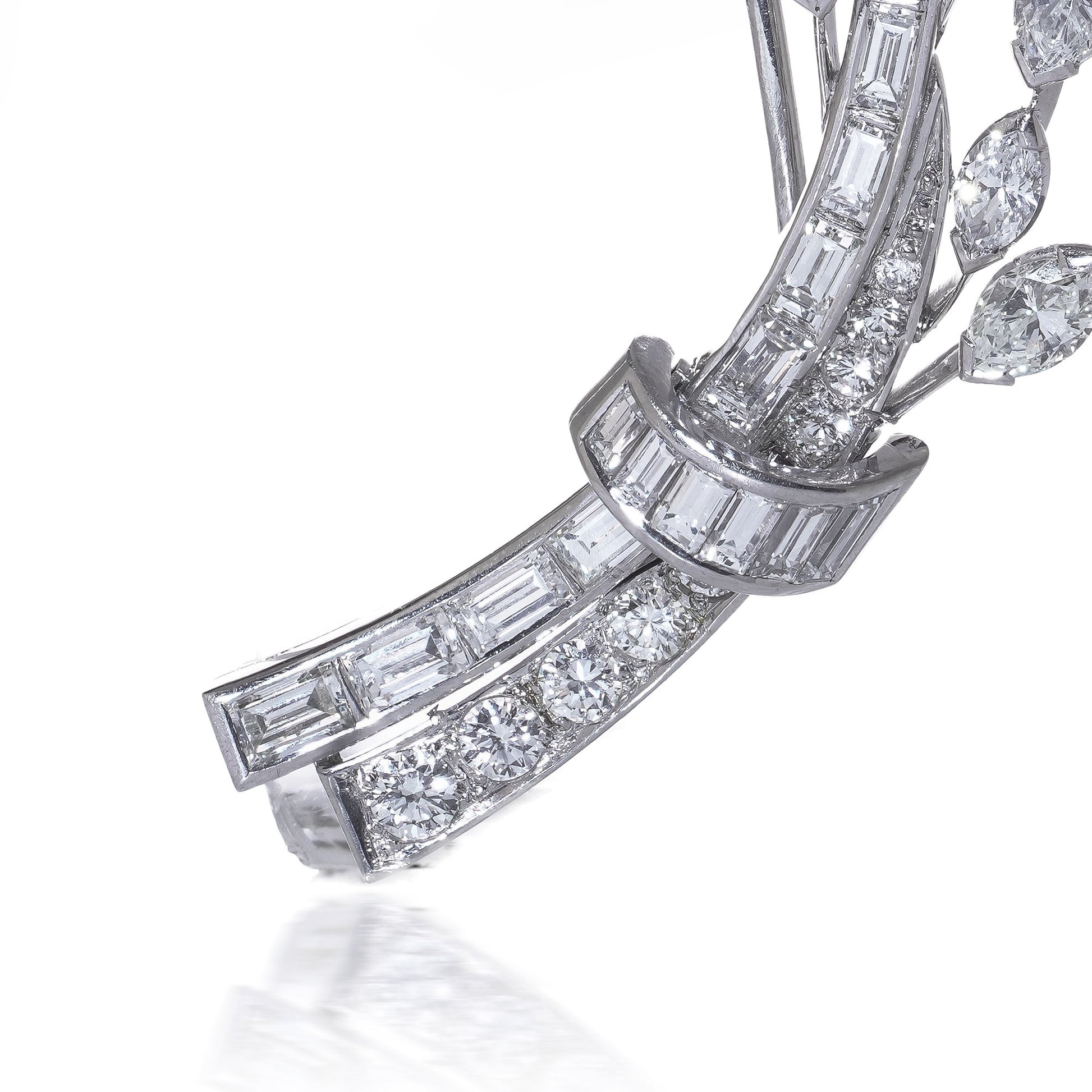 A leaf design brooch set with baguette, marquise and brilliant cut diamonds in white metal, on a white background