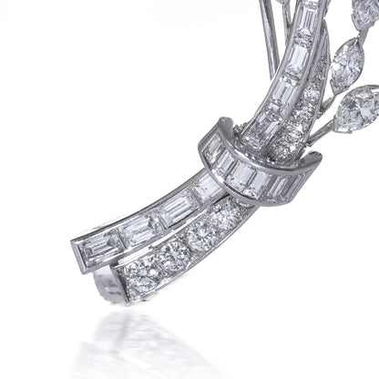 A leaf design brooch set with baguette, marquise and brilliant cut diamonds in white metal, on a white background