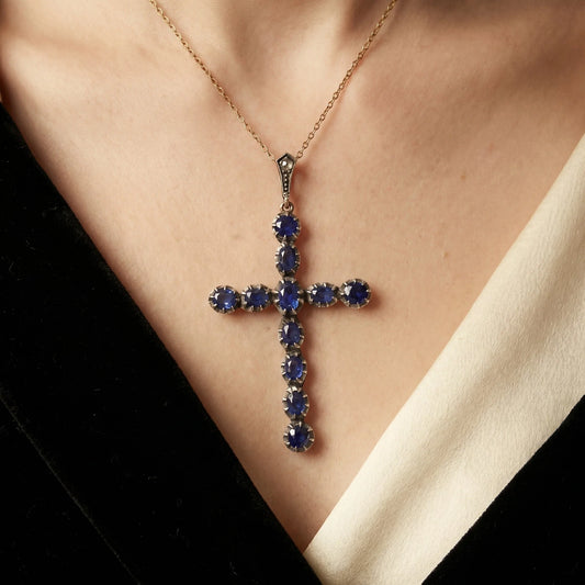 An oval blue sapphire cross pendant in silver and yellow gold, with a chain, modelled