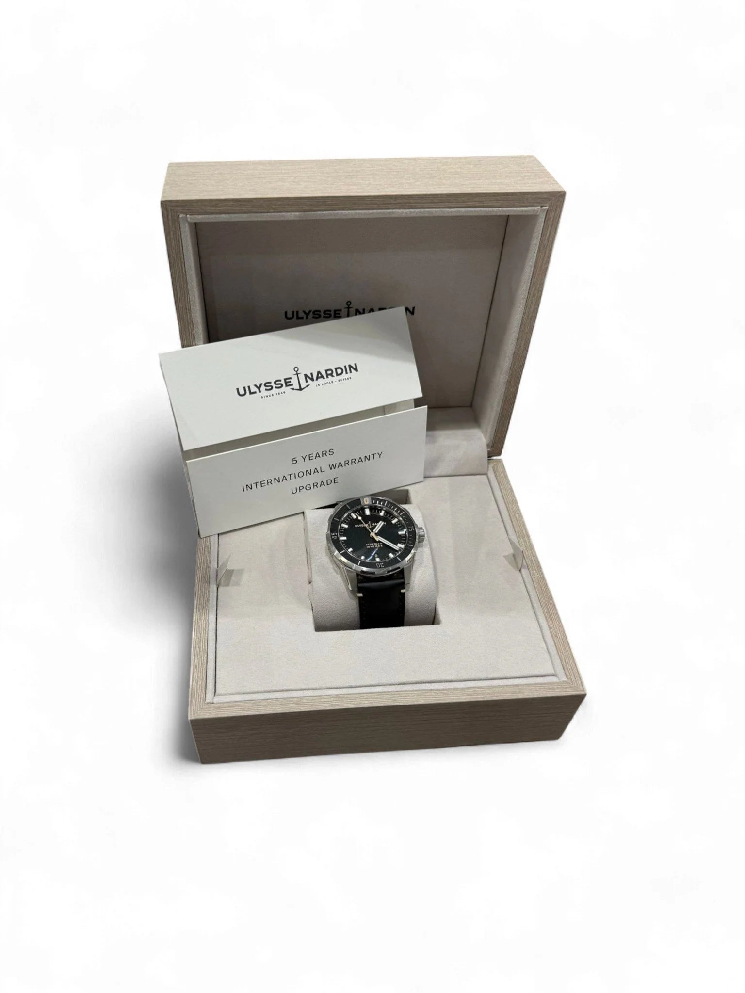 Ulysse Nardin stainless steel watch with black leather strap, in a box with papers, on a white background