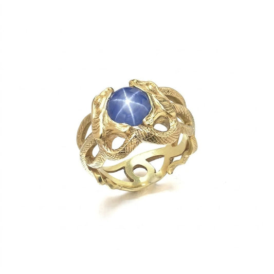 A yellow gold double snake ring holding a cabochon star sapphire in their mouths