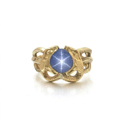 A yellow gold double snake ring holding a cabochon star sapphire in their mouths