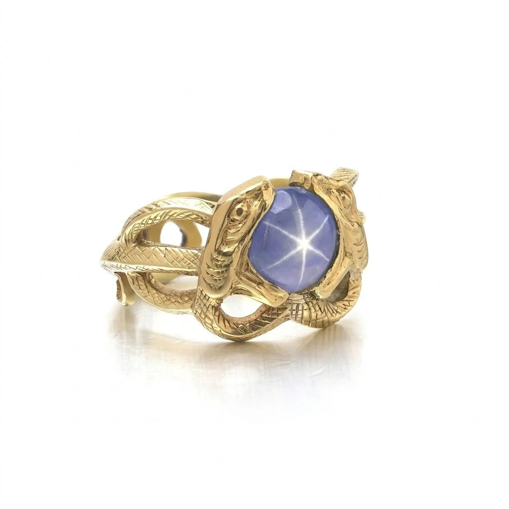 A yellow gold double snake ring holding a cabochon star sapphire in their mouths