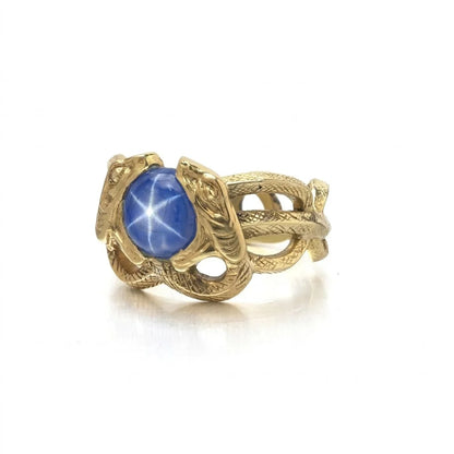 A yellow gold double snake ring holding a cabochon star sapphire in their mouths