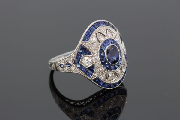 Art Deco Style Sapphire and Diamond Platinum Dress Ring; central oval faceted sapphire within diamond set pierced surround and calibre-cut sapphire outer border