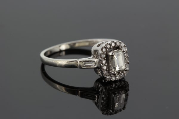 Emerald Cut Diamond Cluster Ring in 18ct White Gold; central 0.52 carat emerald-cut diamond with diamond halo surround and baguette-cut diamond set shoulders