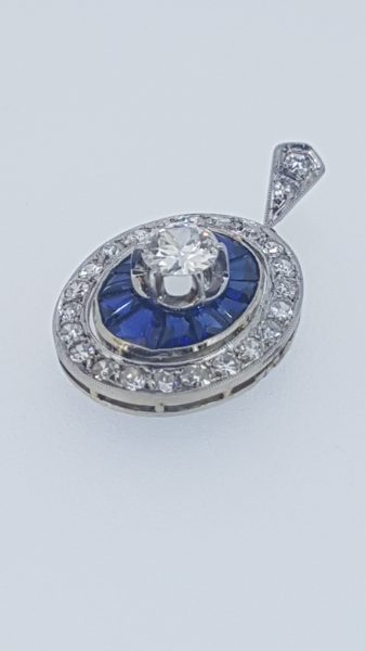 Vintage Calibre Cut Sapphire and Diamond Pendant; central 0.75 carat diamond surrounded by calibre-cut sapphires and outer border of diamonds, diamond set bale, in 18ct white gold, Circa 1960s