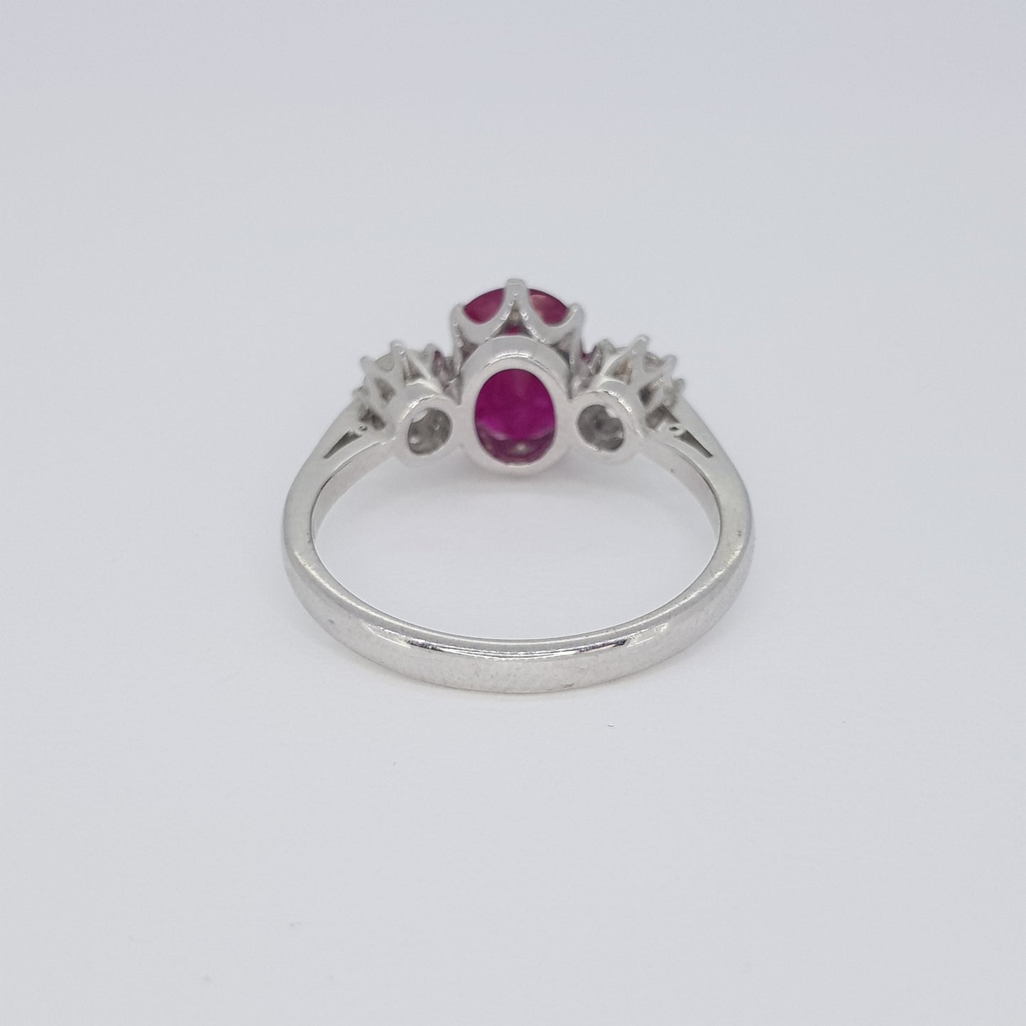 An oval ruby and brilliant cut diamond three stone ring in white metal, against a white background