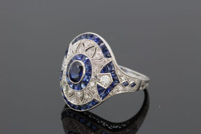 Art Deco Style Sapphire and Diamond Platinum Dress Ring; central oval faceted sapphire within diamond set pierced surround and calibre-cut sapphire outer border