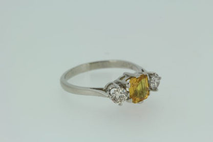 Yellow Sapphire and Diamond Three Stone Ring in Platinum; central 1.25ct octagonal step-cut yellow sapphire flanked by 0.55cts brilliant-cut diamonds