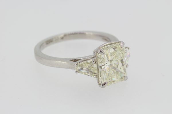 Radiant Emerald Cut Diamond Engagement Ring in Platinum; central 3.02ct emerald radiant-cut diamond, claw set and flanked by 0.43cts shield-shaped trapeze-cut diamonds