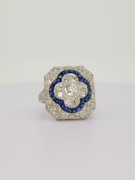 Sapphire and Diamond Cluster Dress Ring; central diamond floral cluster with calibre sapphire border, all within a diamond surround, in 18ct white gold