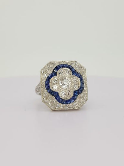 Sapphire and Diamond Cluster Dress Ring; central diamond floral cluster with calibre sapphire border, all within a diamond surround, in 18ct white gold