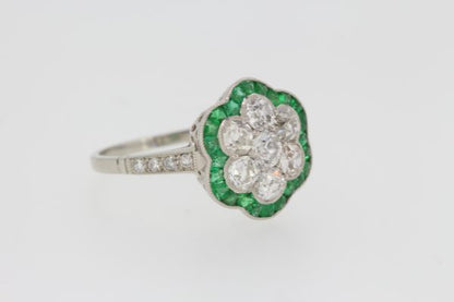 Contemporary Emerald and Diamond Floral Cluster Ring in Platinum; central seven brilliant-cut diamonds flower cluster surrounded by calibre-cut emeralds, with diamond-set shoulders