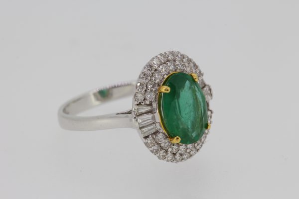 Contemporary Emerald and Diamond Cluster Ring; featuring a 2.20ct oval emerald within a double diamond surround with baguette-cut diamonds to the sides, in 18ct white gold