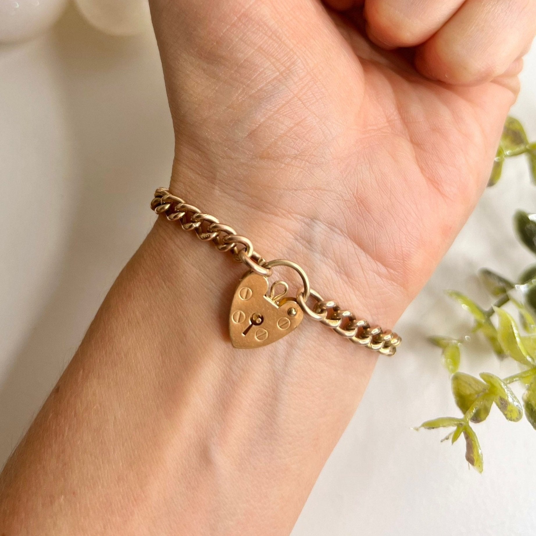 A gold curb link bracelet with a heart-shaped padlock clasp, modelled on a wrist