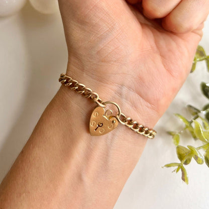 A gold curb link bracelet with a heart-shaped padlock clasp, modelled on a wrist