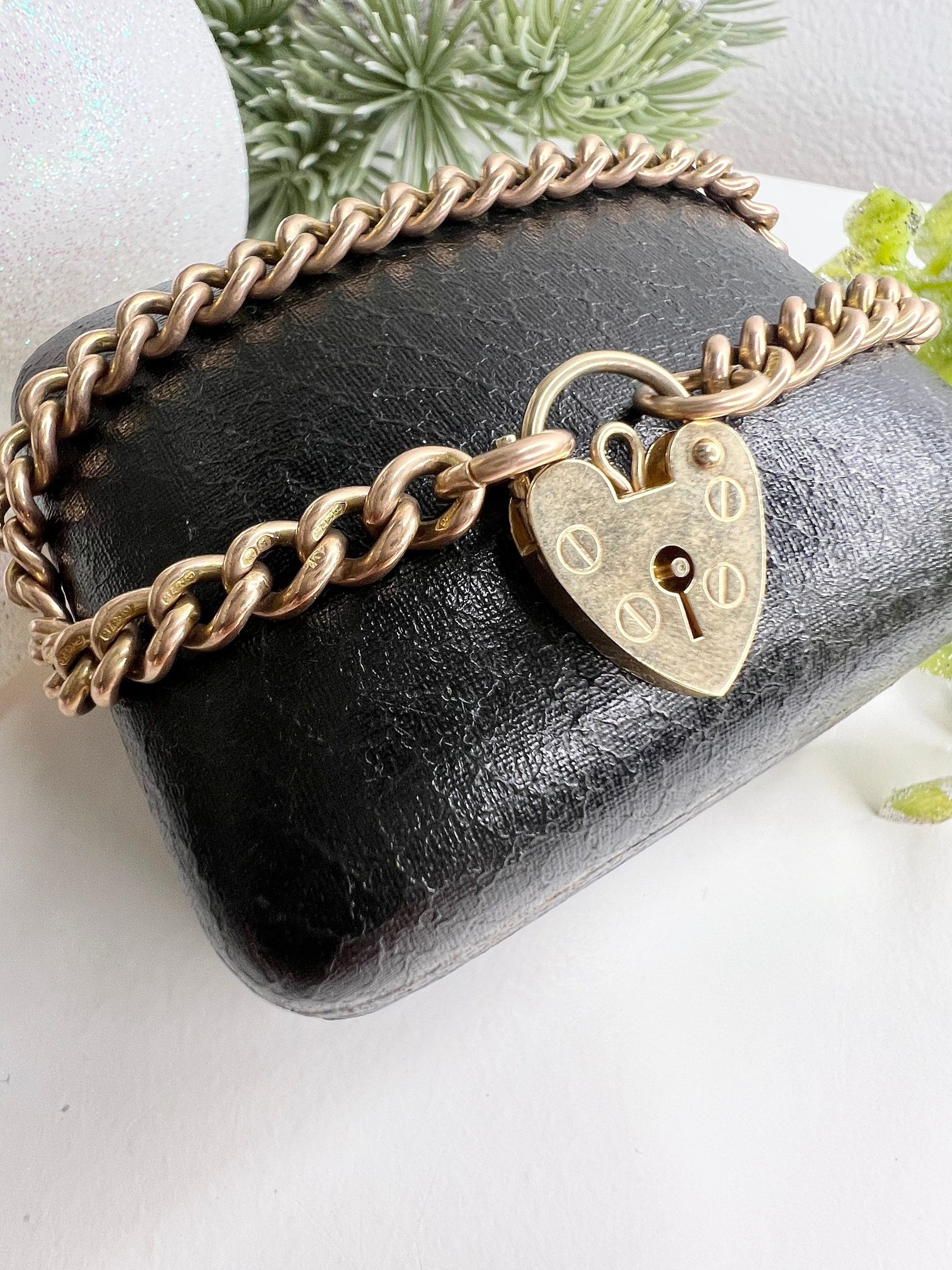 A gold curb link bracelet with a heart-shaped padlock clasp