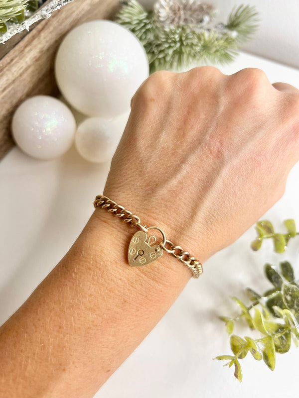 A gold curb link bracelet with a heart-shaped padlock clasp, modelled on a wrist
