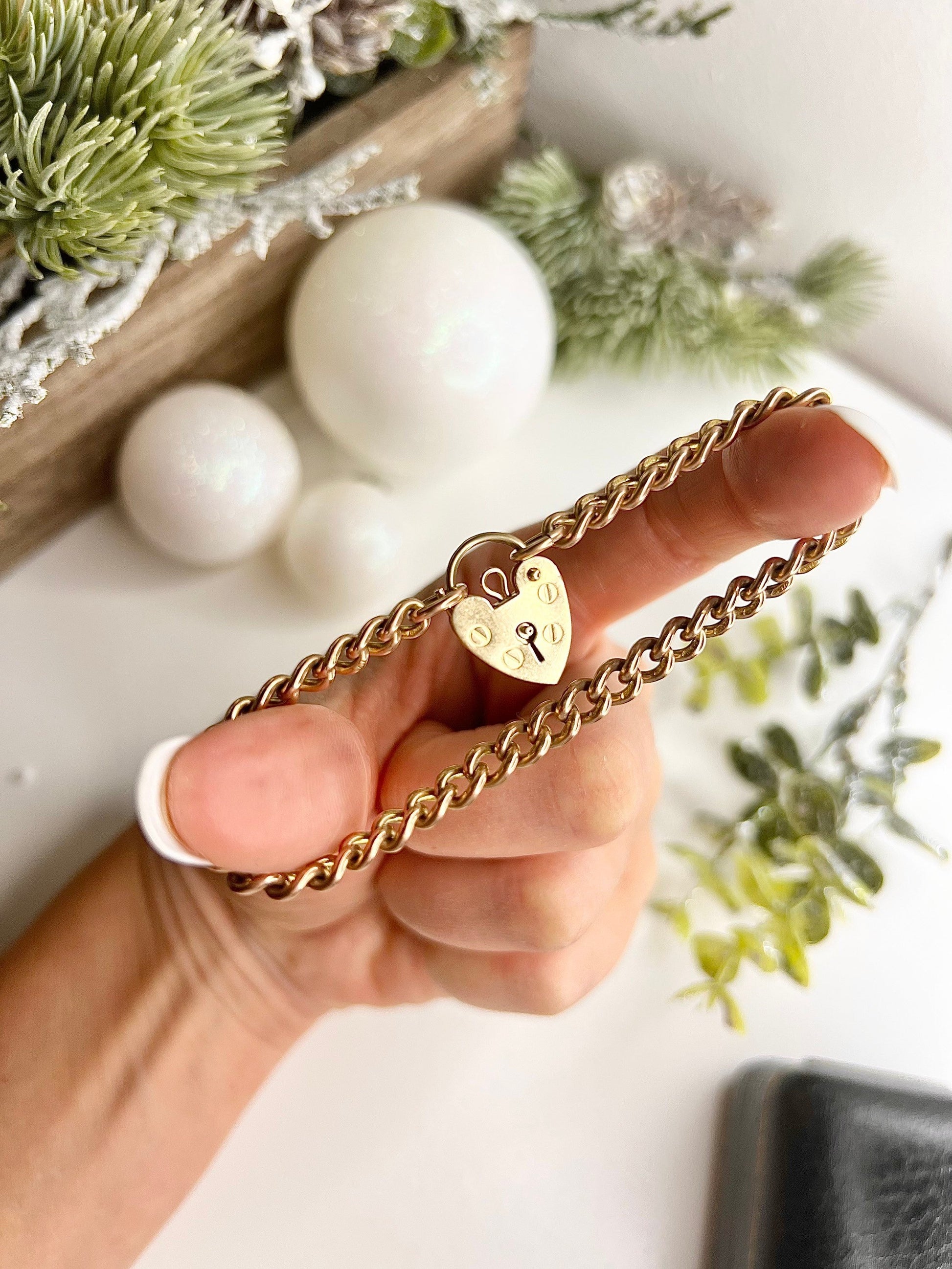 A gold curb link bracelet with a heart-shaped padlock clasp, held in a hand