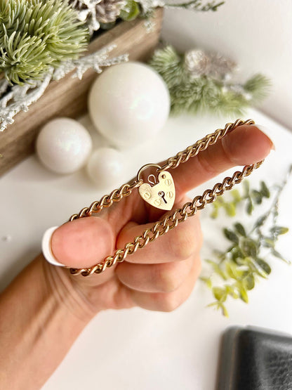A gold curb link bracelet with a heart-shaped padlock clasp, held in a hand
