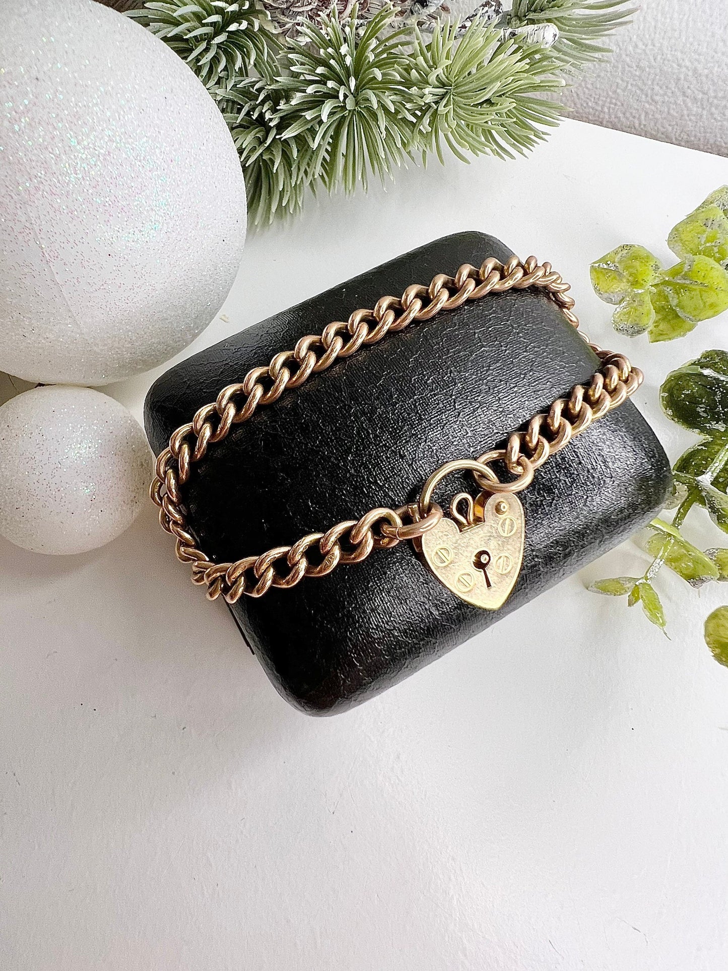 A gold curb link bracelet with a heart-shaped padlock clasp