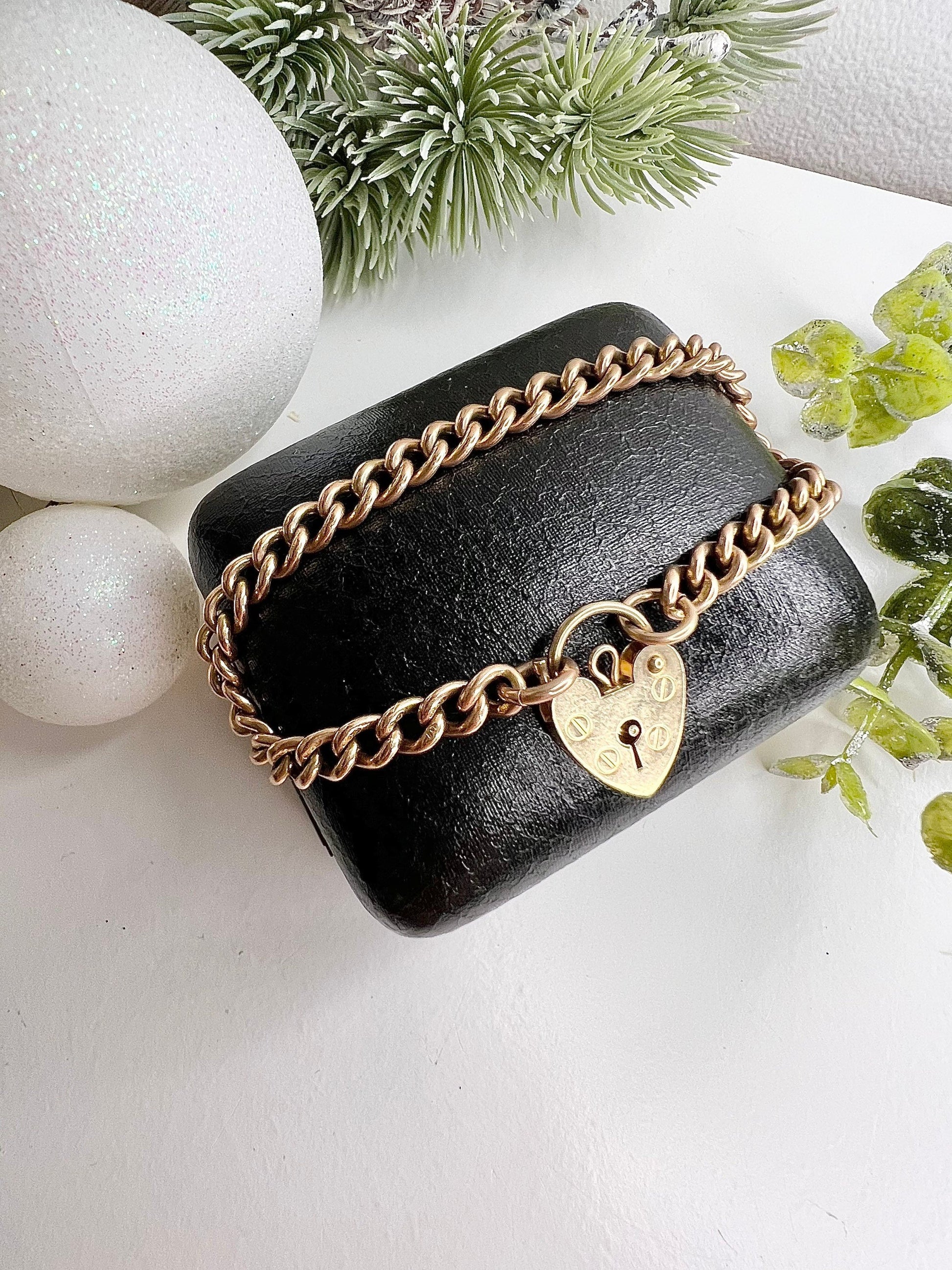 A gold curb link bracelet with a heart-shaped padlock clasp