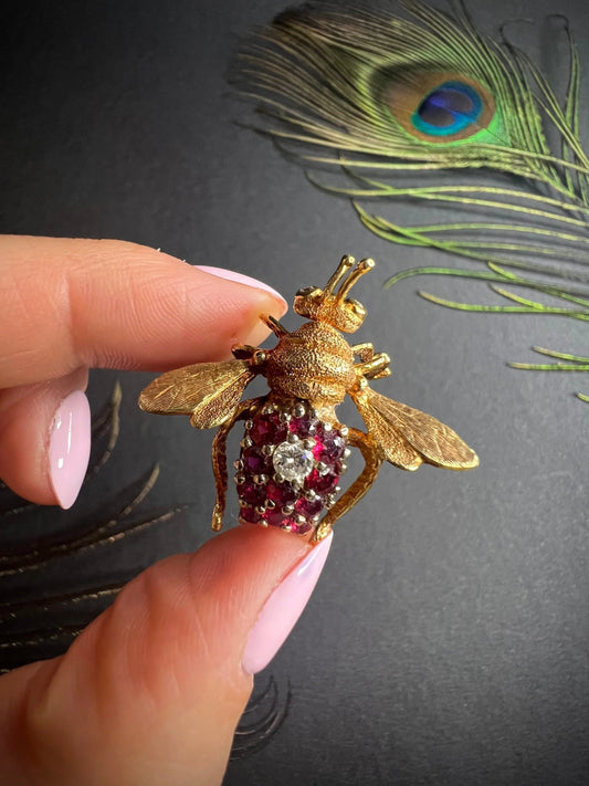 A ruby and diamond yellow gold bee brooch, held in a hand