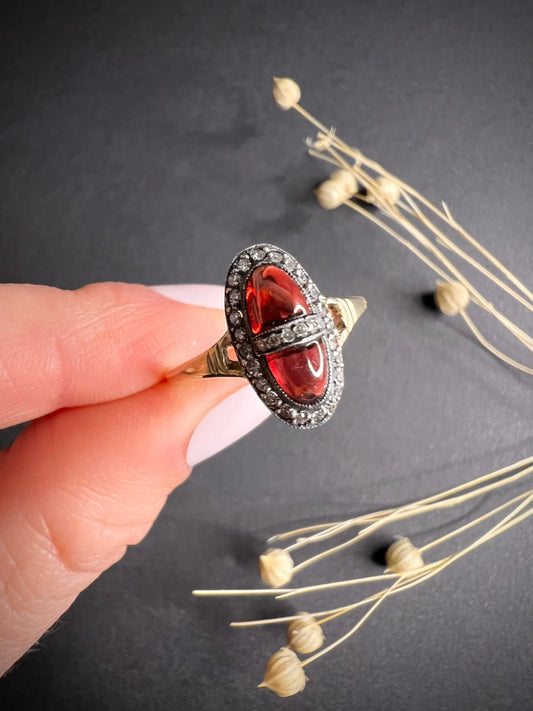 An oval cabochon garnet and diamond ring in yellow gold and platinum, held in a hand