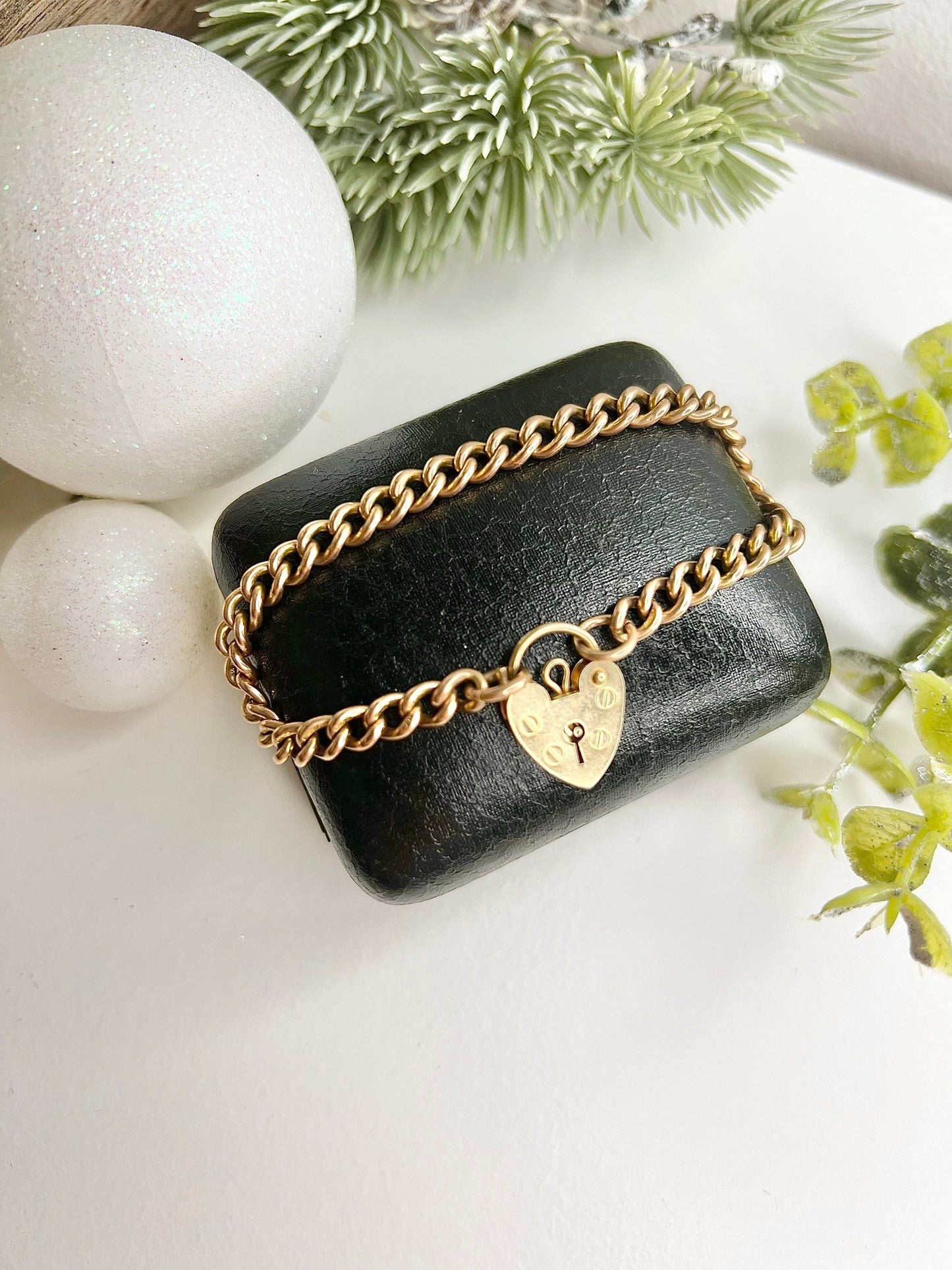 A gold curb link bracelet with a heart-shaped padlock clasp