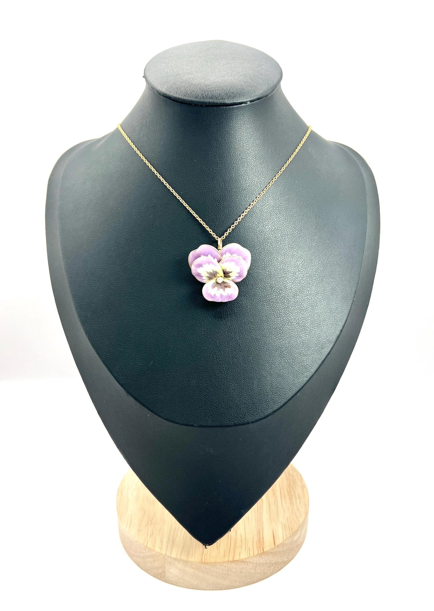 An enamelled pansy flower pendant/brooch with a diamond centre, in yellow gold, with a chain, on a black jewellery bust