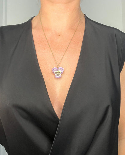 An enamelled pansy flower pendant/brooch with a diamond centre, in yellow gold, with a chain, modelled by a woman wearing a black top