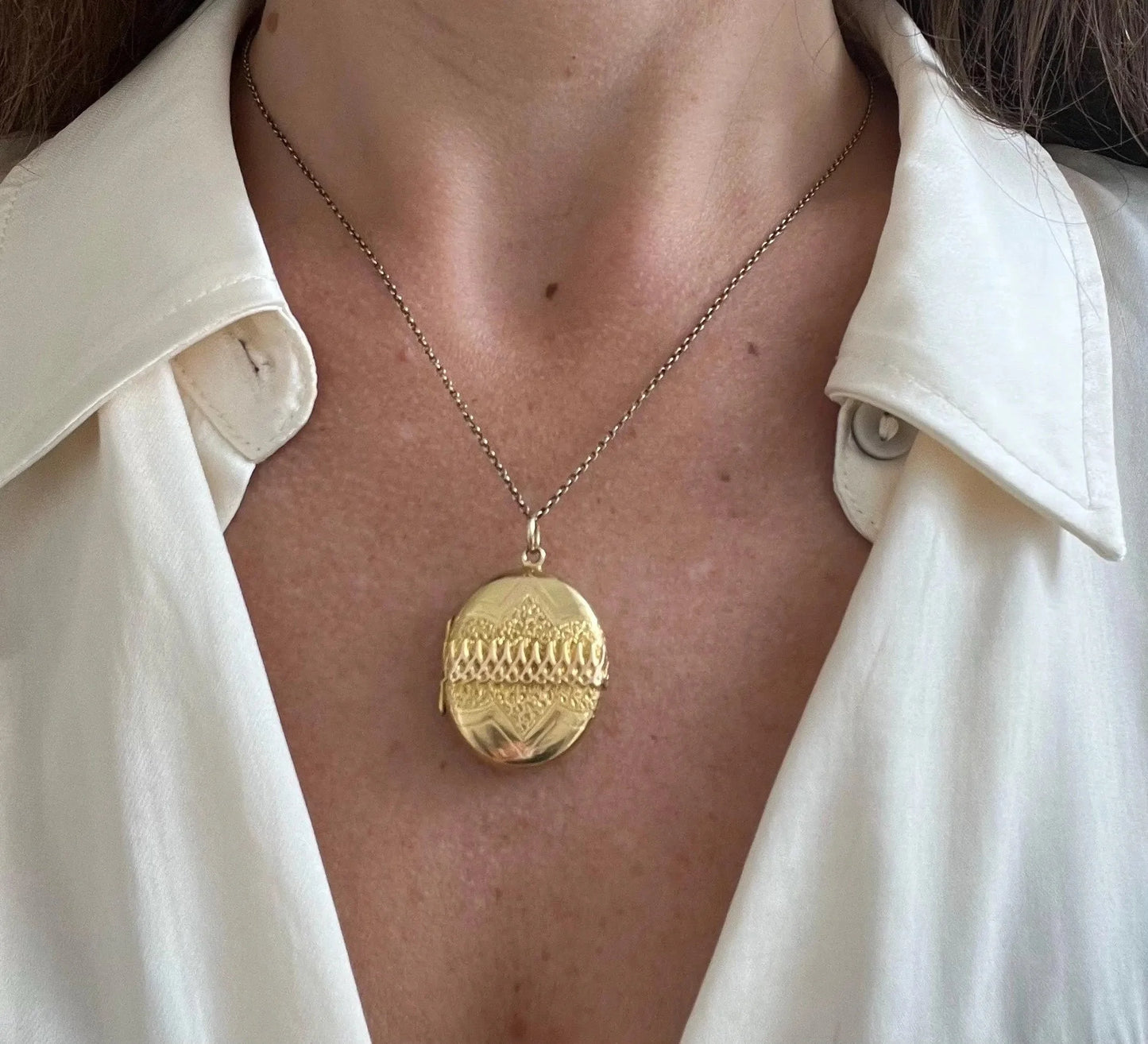 A yellow gold oval patterned locket pendant, with a chain, modelled by a woman