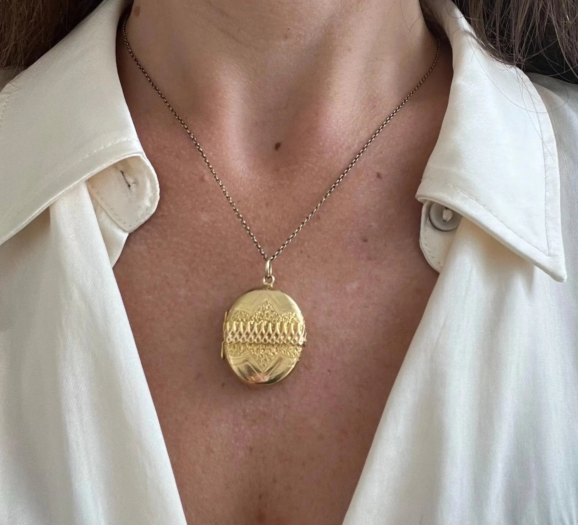 A yellow gold oval patterned locket pendant, with a chain, modelled by a woman