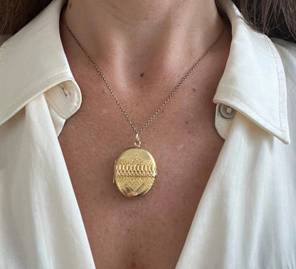 A yellow gold oval patterned locket pendant, with a chain, modelled by a woman