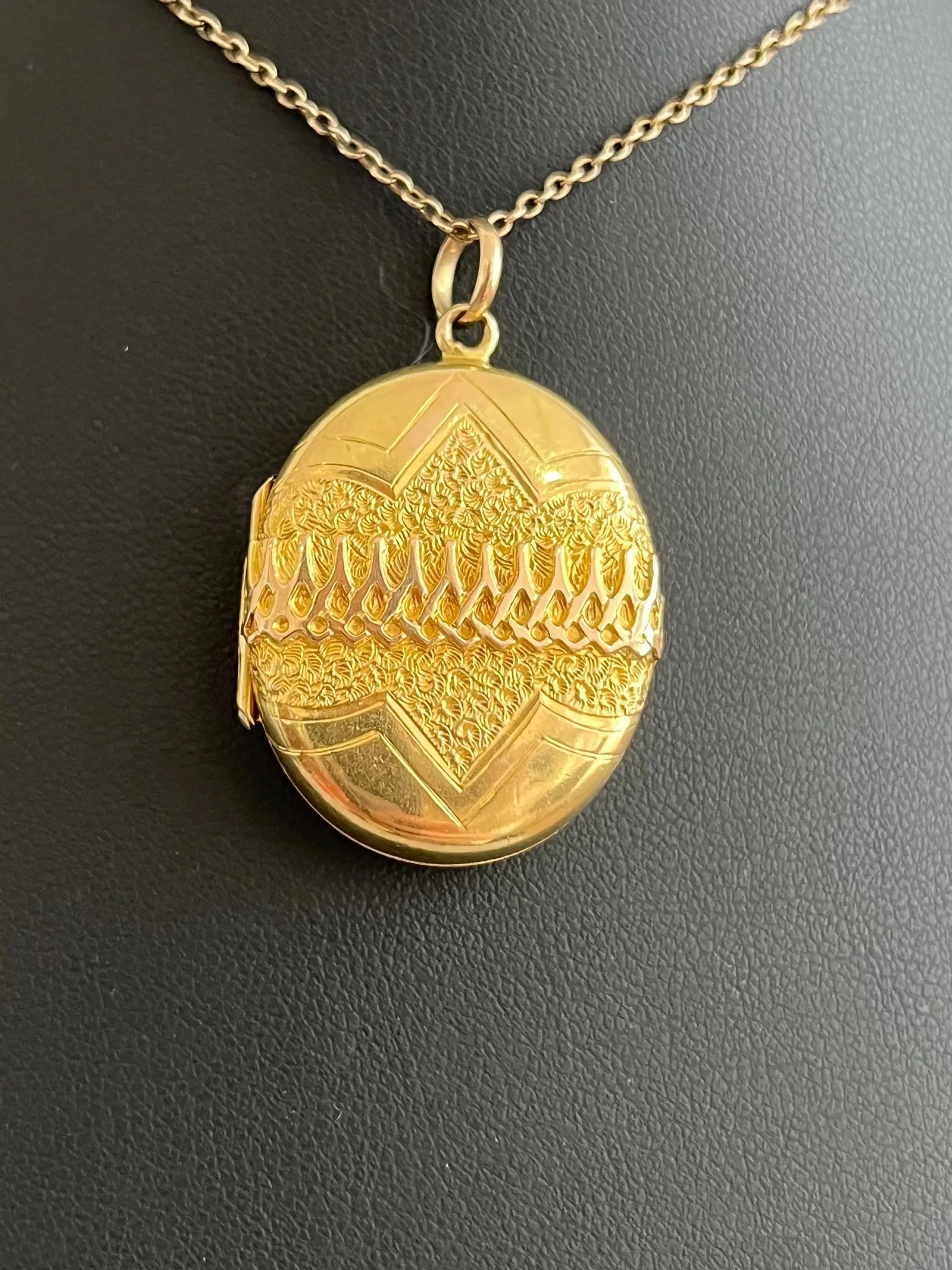 A yellow gold oval patterned locket pendant, with a chain