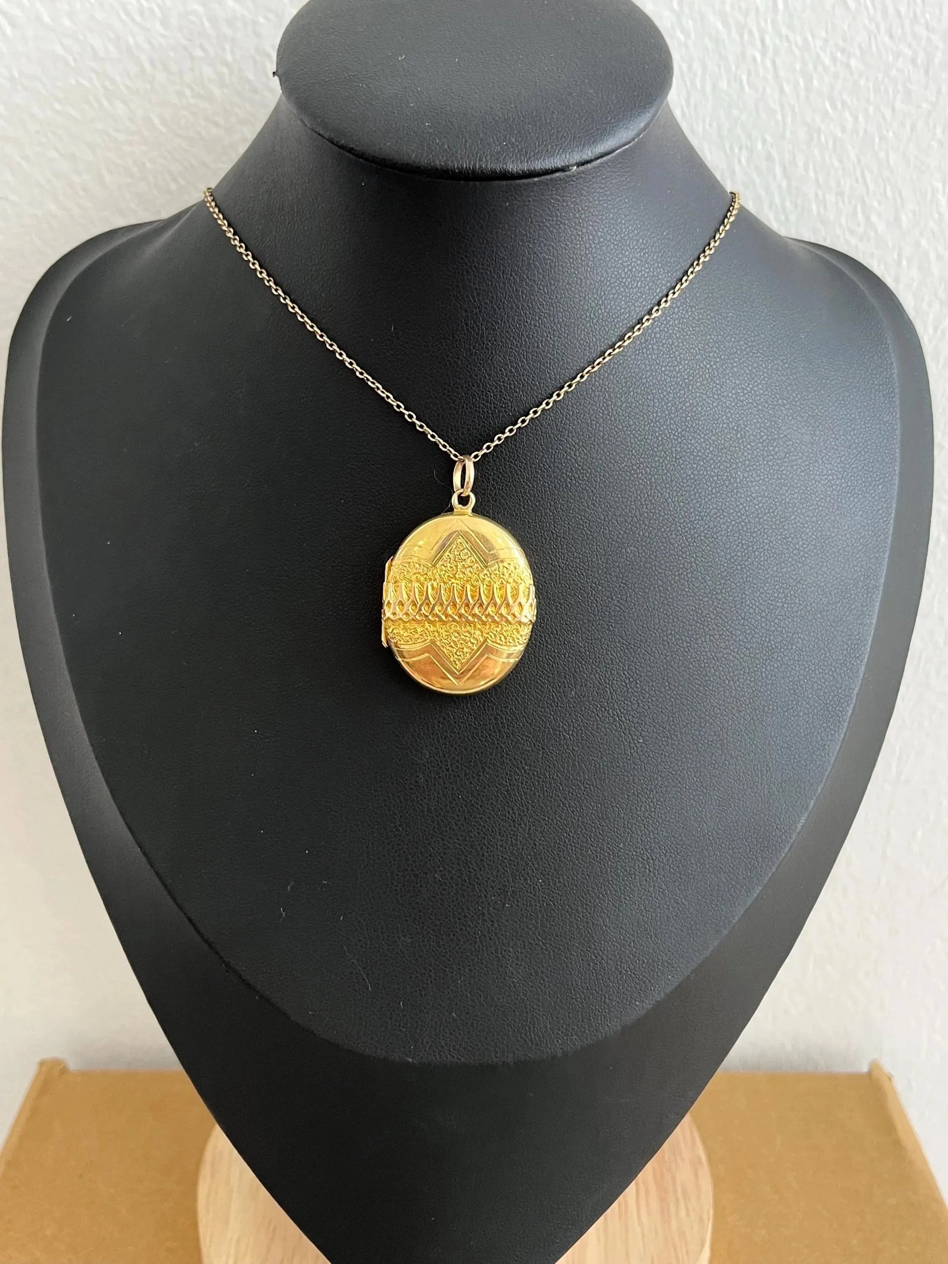 A yellow gold oval patterned locket pendant, with a chain, on a black bust