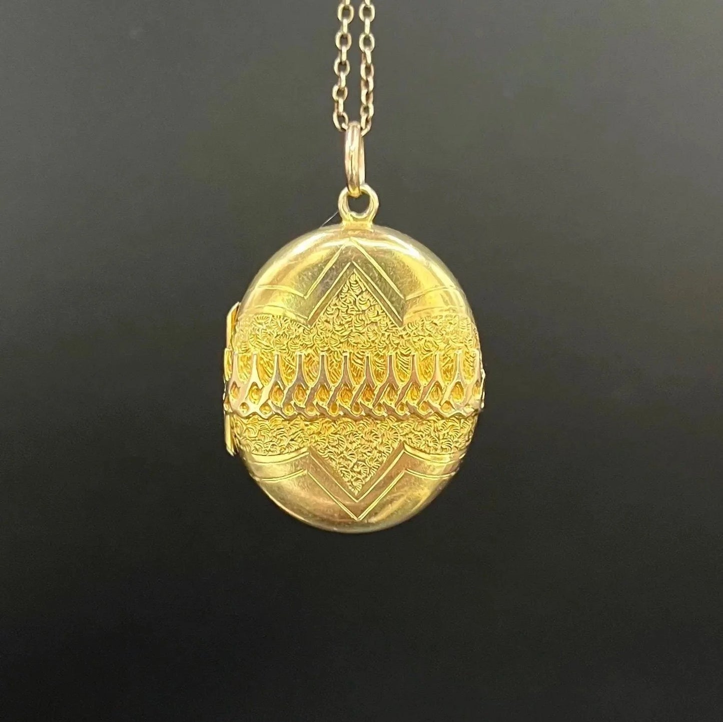 A yellow gold oval patterned locket pendant, with a chain