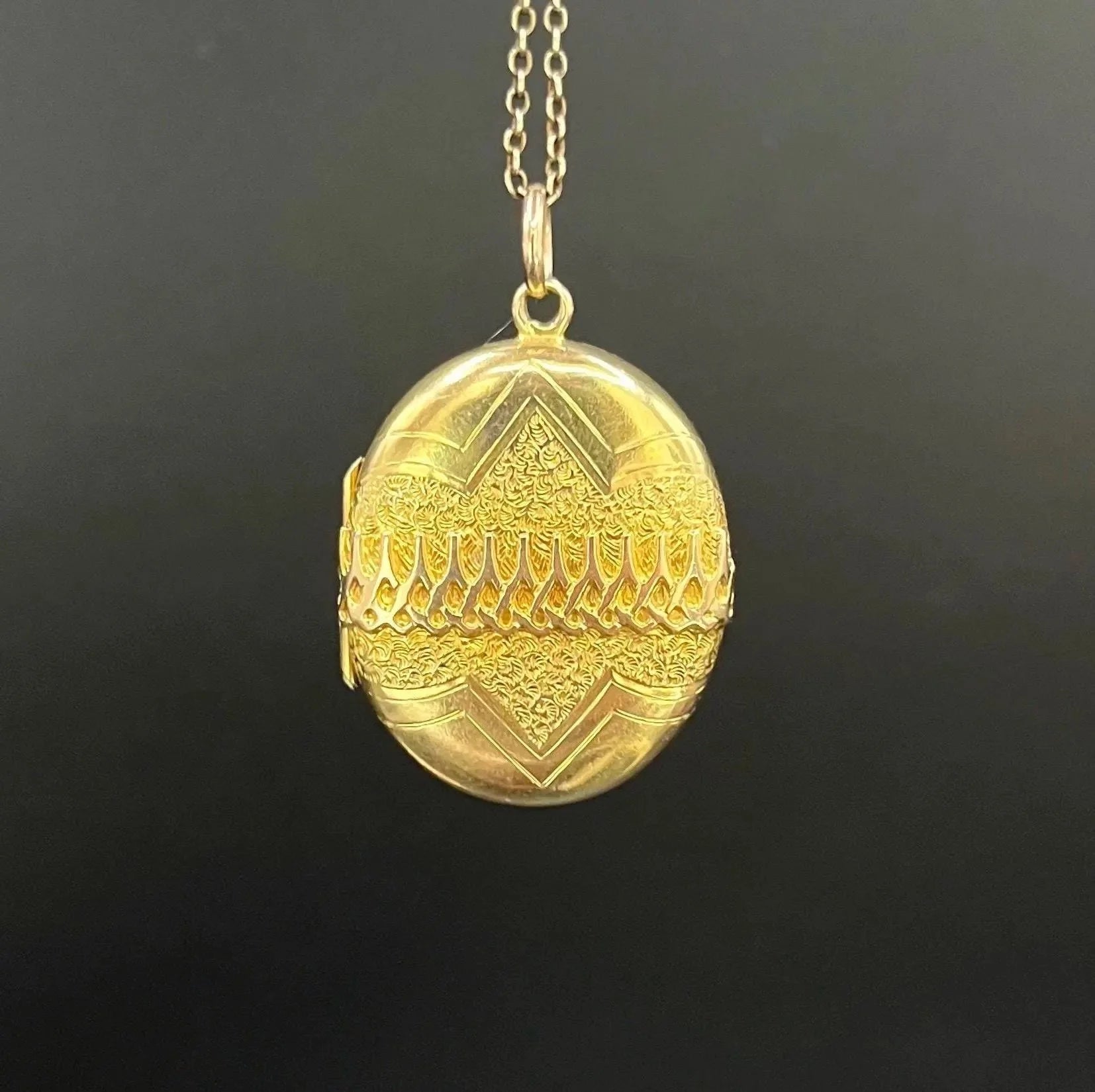 A yellow gold oval patterned locket pendant, with a chain